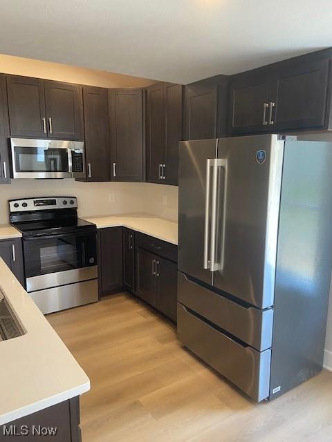 kitchen featuring light countertops, dark brown cabinetry, appliances with stainless steel finishes, and light wood-style floors
