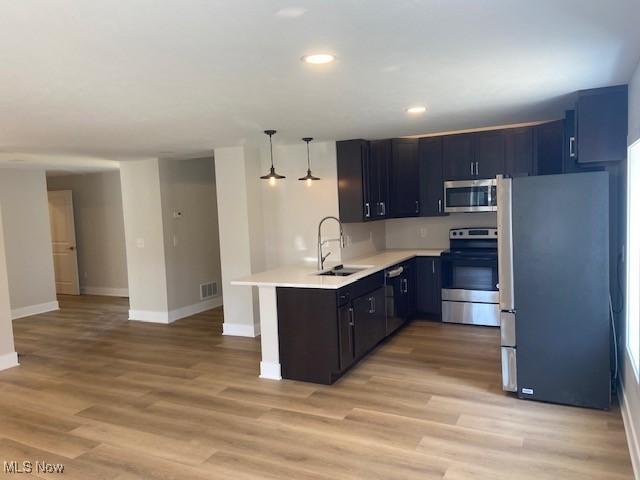 kitchen with appliances with stainless steel finishes, light countertops, a sink, baseboards, and a peninsula