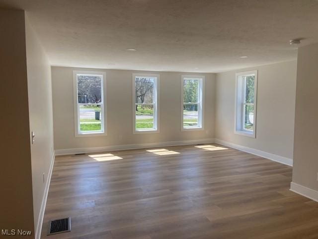 empty room with baseboards, visible vents, and wood finished floors