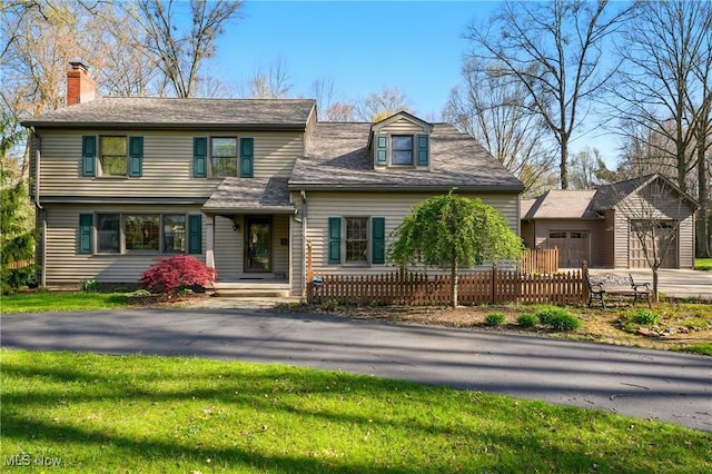 view of front of property featuring a chimney, fence private yard, an outbuilding, driveway, and a front yard
