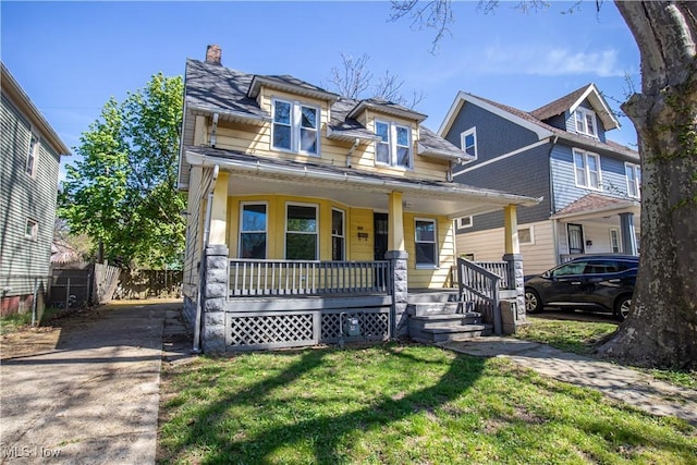 view of front of house featuring a porch, a front yard, fence, and a chimney