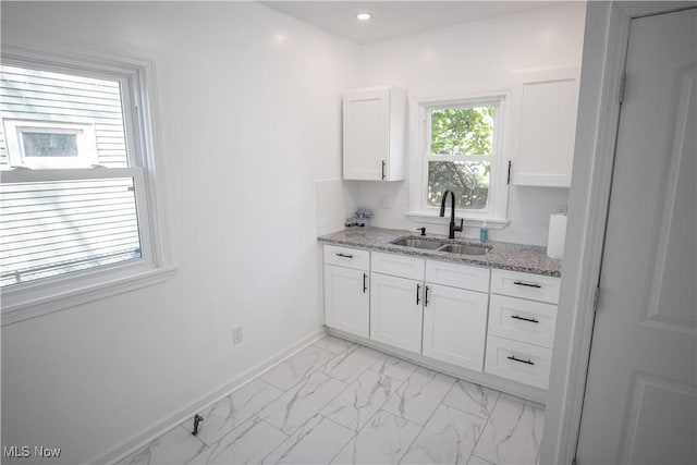 kitchen featuring marble finish floor, a sink, white cabinets, and baseboards