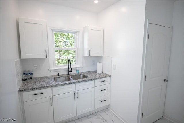 kitchen with marble finish floor, a sink, white cabinetry, and light stone countertops