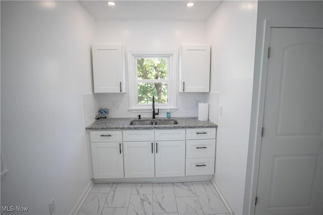 kitchen featuring baseboards, marble finish floor, light stone counters, and a sink