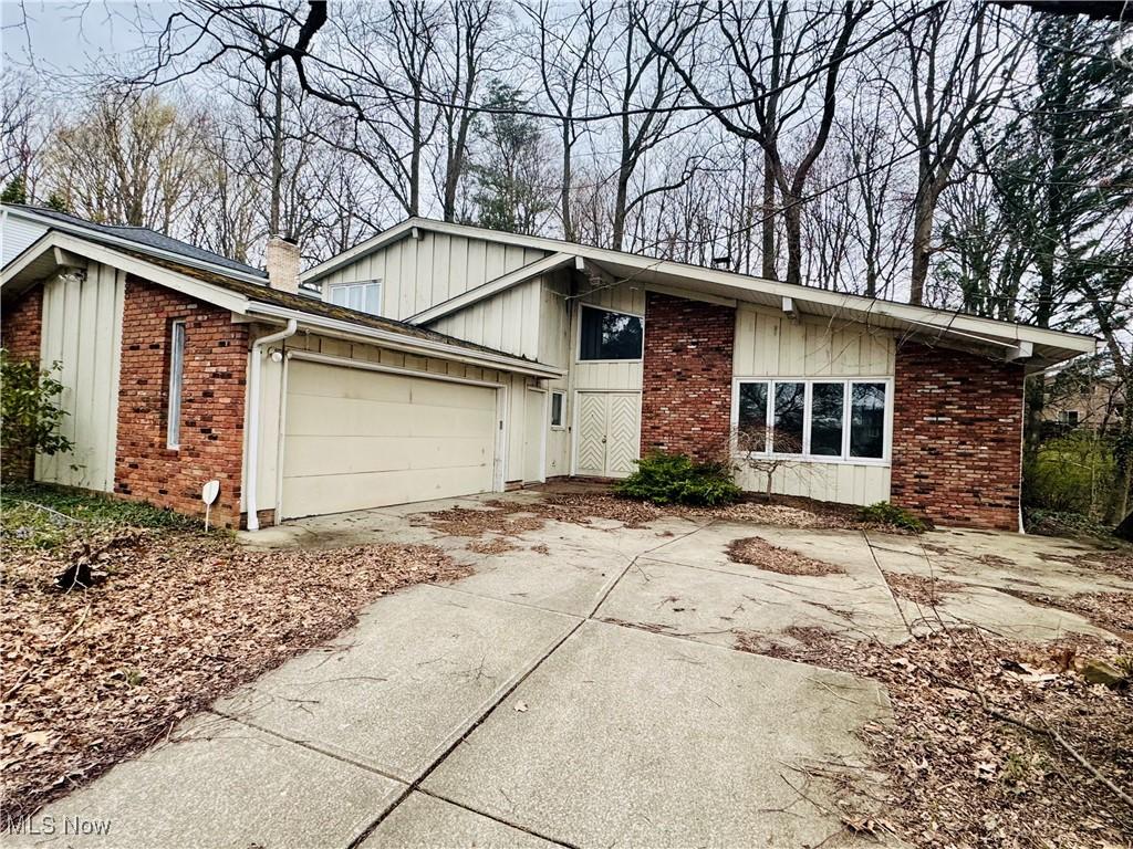 view of front of home featuring concrete driveway, board and batten siding, a chimney, brick siding, and a garage