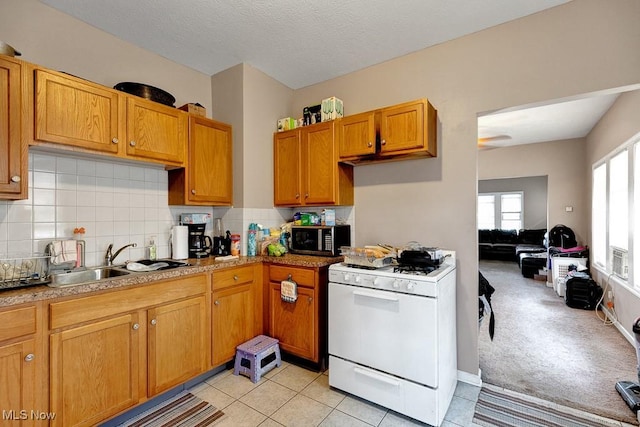 kitchen featuring stainless steel microwave, tasteful backsplash, white range with gas stovetop, and a sink