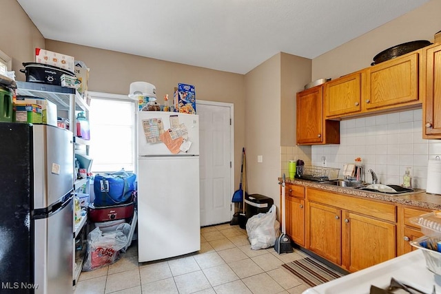kitchen with light tile patterned flooring, decorative backsplash, freestanding refrigerator, and a sink
