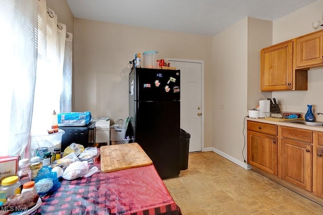 kitchen with brown cabinetry, a sink, light countertops, and freestanding refrigerator