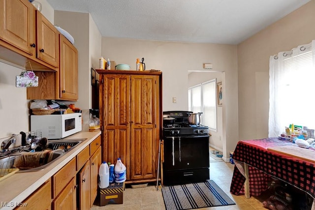 kitchen with brown cabinets, a sink, black gas stove, light countertops, and white microwave