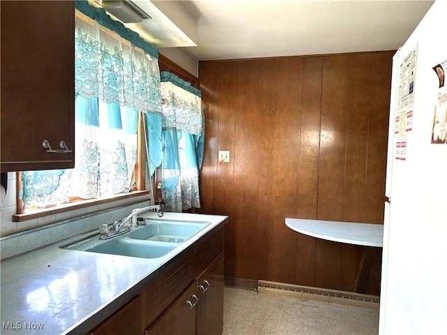 kitchen featuring wooden walls, a sink, baseboard heating, and freestanding refrigerator