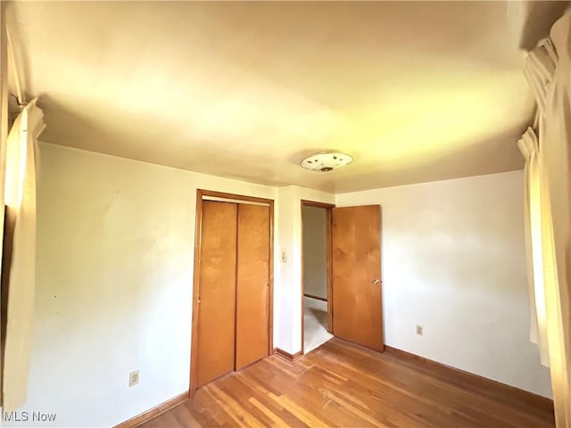 unfurnished bedroom featuring a closet, wood finished floors, and baseboards