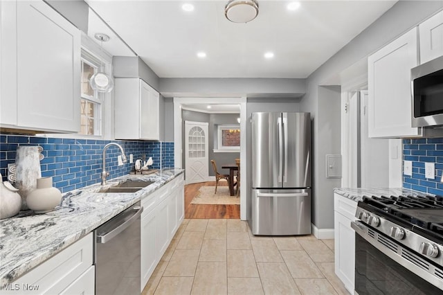 kitchen with light stone countertops, a wealth of natural light, appliances with stainless steel finishes, a sink, and white cabinetry