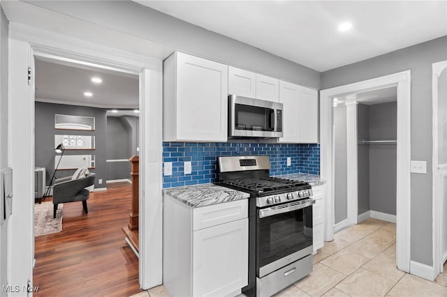 kitchen featuring white cabinetry, decorative backsplash, stainless steel appliances, baseboards, and light stone countertops