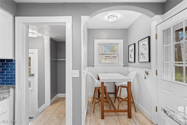 dining area featuring light tile patterned floors, a wainscoted wall, arched walkways, and a healthy amount of sunlight