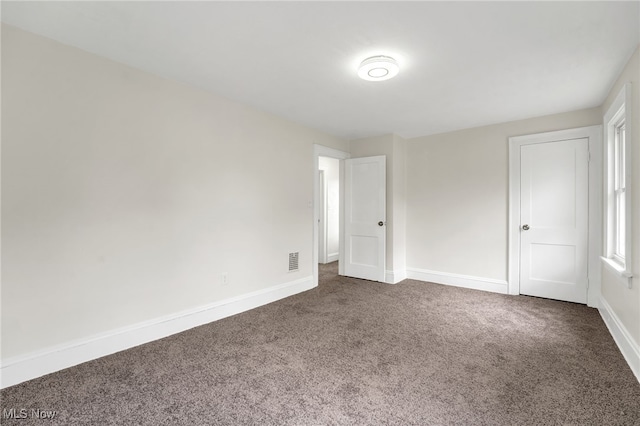 spare room featuring dark carpet, visible vents, and baseboards