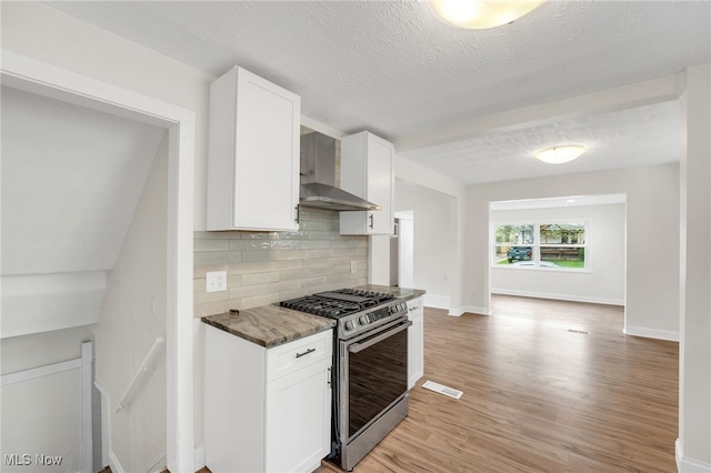 kitchen with light wood-style flooring, backsplash, white cabinetry, stainless steel gas range, and wall chimney exhaust hood
