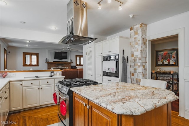 kitchen with light stone countertops, oven, a kitchen island, stainless steel gas stove, and island range hood