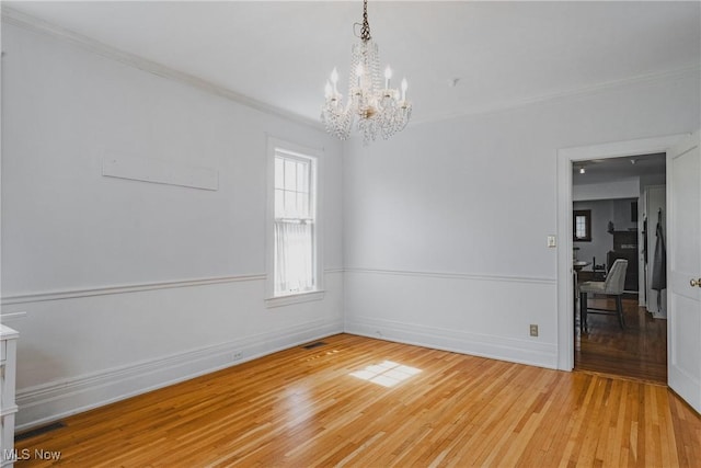 unfurnished room featuring ornamental molding, an inviting chandelier, light wood-style flooring, and baseboards