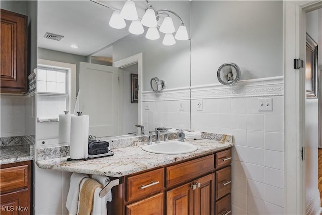 bathroom with a wainscoted wall, tile walls, visible vents, and vanity