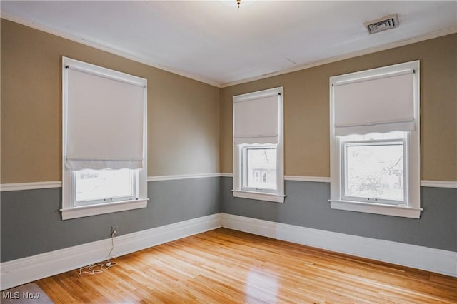 spare room with visible vents, wood finished floors, a healthy amount of sunlight, and ornamental molding