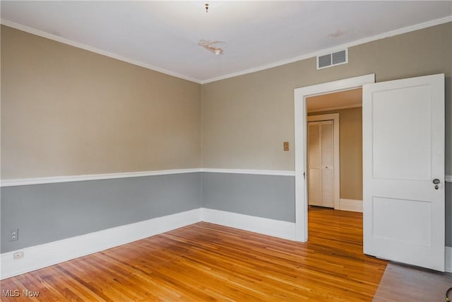 empty room with baseboards, visible vents, wood finished floors, and crown molding
