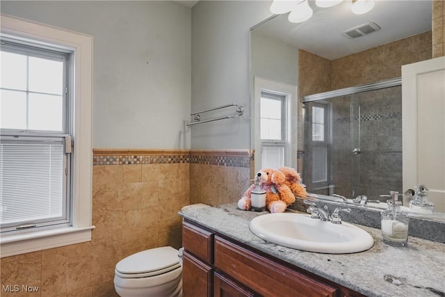 full bathroom with a shower stall, tile walls, toilet, vanity, and visible vents