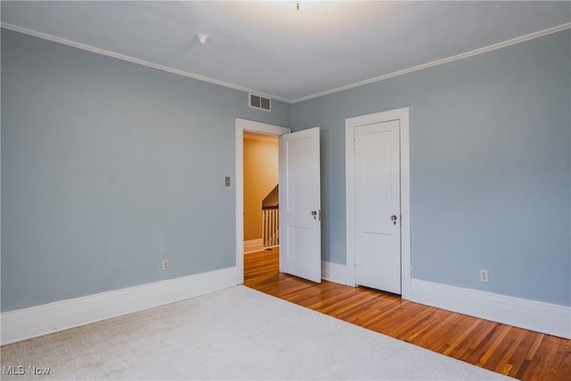 unfurnished bedroom with baseboards, visible vents, ornamental molding, and wood finished floors