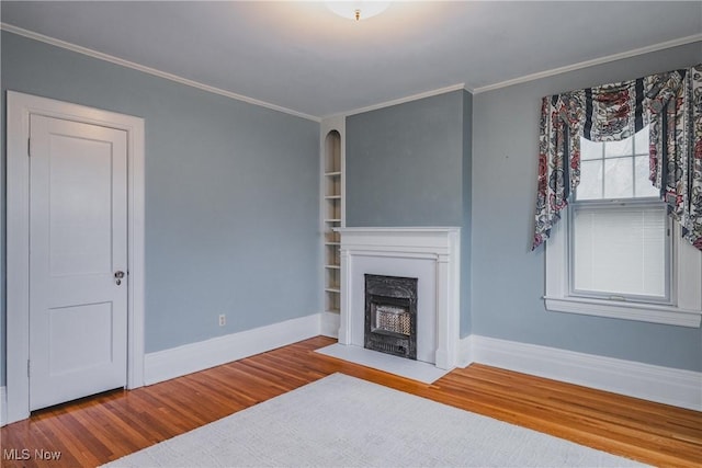 unfurnished living room featuring a fireplace with flush hearth, built in shelves, baseboards, ornamental molding, and wood finished floors