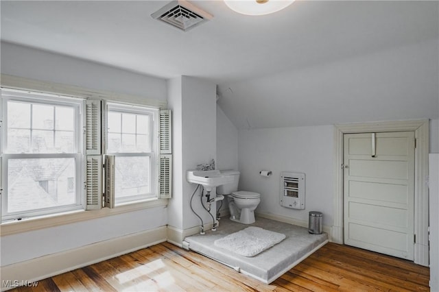 bathroom featuring visible vents, heating unit, wood finished floors, and vaulted ceiling