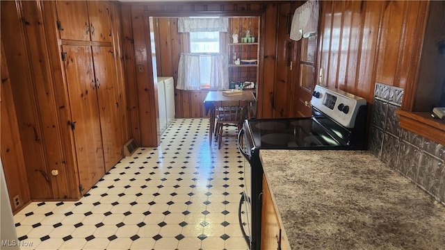 kitchen with electric stove, brown cabinetry, visible vents, wood walls, and light floors