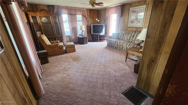 carpeted living room with visible vents, a ceiling fan, and wooden walls
