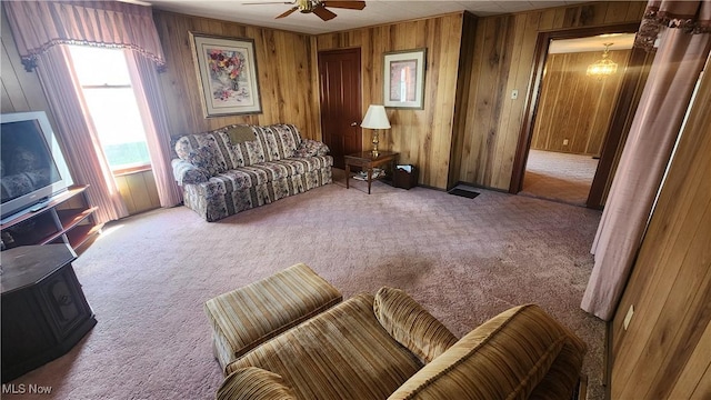 carpeted living area with wood walls and ceiling fan