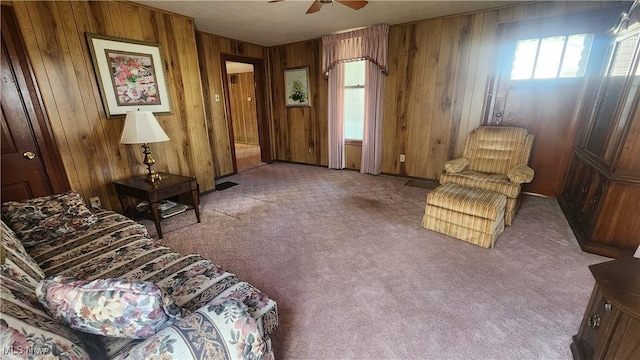 carpeted living area featuring wooden walls and ceiling fan