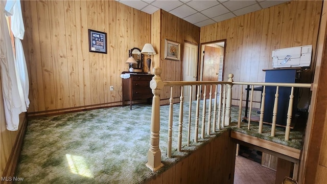 interior space with a paneled ceiling, carpet flooring, wood walls, and baseboards