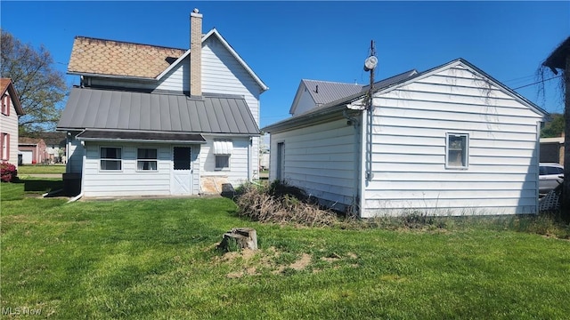 back of property featuring metal roof, a lawn, and a chimney