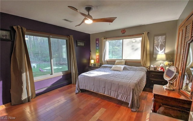 bedroom featuring baseboard heating, visible vents, wood finished floors, and a ceiling fan