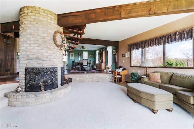 living area featuring ceiling fan, a fireplace, carpet flooring, and beam ceiling