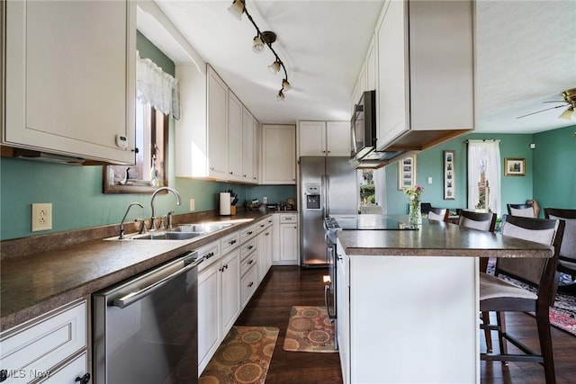 kitchen featuring appliances with stainless steel finishes, dark countertops, a sink, a breakfast bar, and dark wood-type flooring