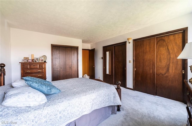 bedroom featuring two closets, a textured ceiling, and light colored carpet