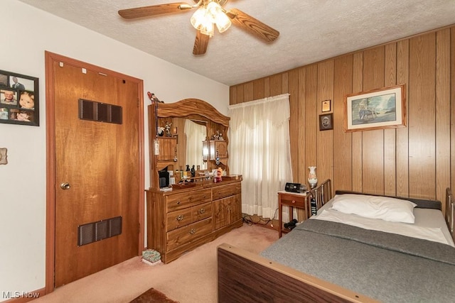 bedroom featuring a textured ceiling, wood walls, light colored carpet, visible vents, and a ceiling fan