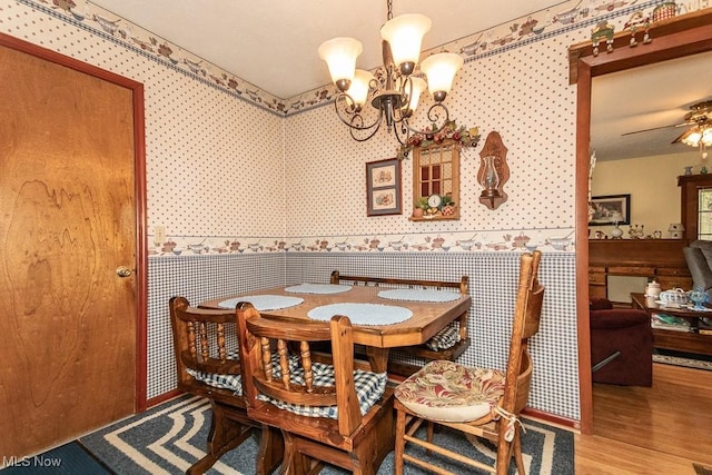 dining space with wallpapered walls, a wainscoted wall, an inviting chandelier, and wood finished floors