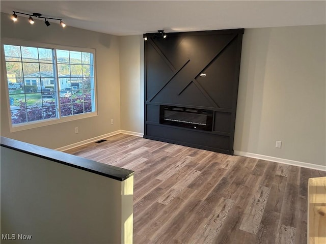 unfurnished living room featuring baseboards, visible vents, wood finished floors, and rail lighting
