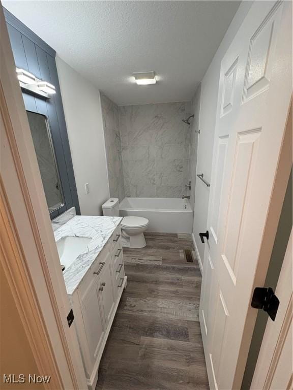 full bathroom with shower / tub combination, a textured ceiling, toilet, wood finished floors, and vanity