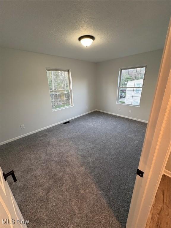 unfurnished room featuring baseboards, visible vents, a textured ceiling, and plenty of natural light