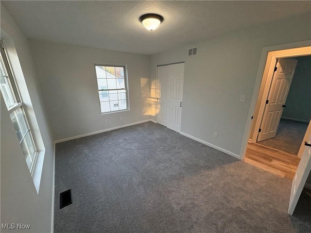 unfurnished bedroom featuring a textured ceiling, dark colored carpet, visible vents, a closet, and baseboards