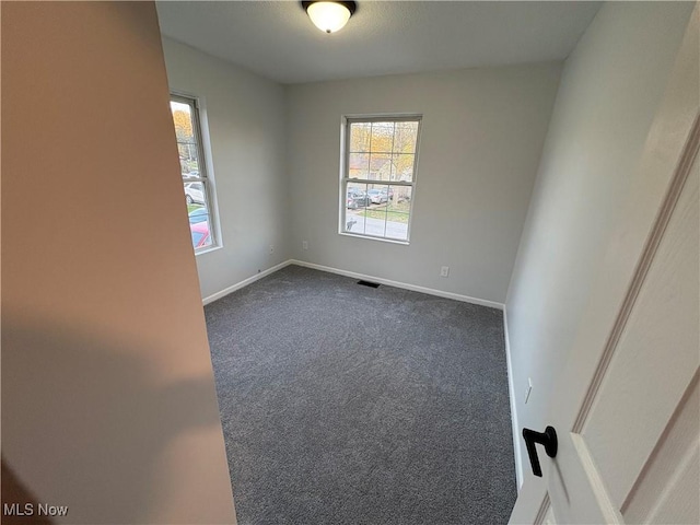 unfurnished room featuring dark carpet, visible vents, and baseboards