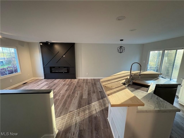 kitchen featuring baseboards, a wealth of natural light, dark wood-style flooring, and a center island with sink
