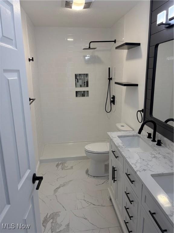 full bath with visible vents, toilet, a tile shower, and a sink