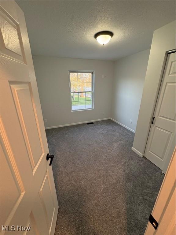 empty room featuring dark carpet, a textured ceiling, visible vents, and baseboards