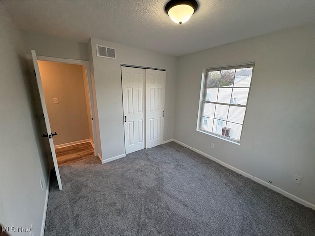 unfurnished bedroom featuring a closet, visible vents, dark carpet, baseboards, and a textured ceiling